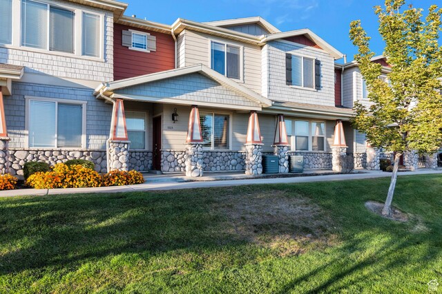view of front facade featuring a front yard, stone siding, and covered porch