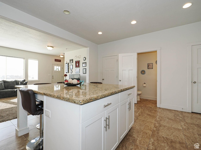 8092 W Rock Creek Cove Ln, Eagle Mountain, UT 84005 - kitchen with open floor plan, a kitchen breakfast bar, white cabinetry, light stone countertops, and a kitchen island