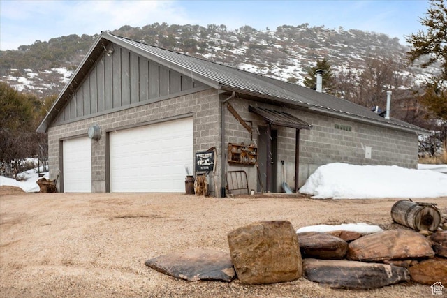 1510 S Mahogany Dr, Garden City, UT 84028 - view of snowy exterior with a mountain view, a detached garage, board and batten siding, concrete block siding, and metal roof