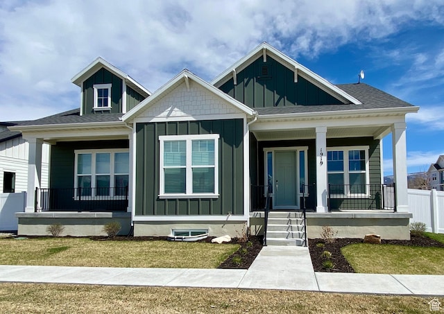 view of front of home featuring roof with shingles, board and batten siding, a front lawn, a porch, and fence