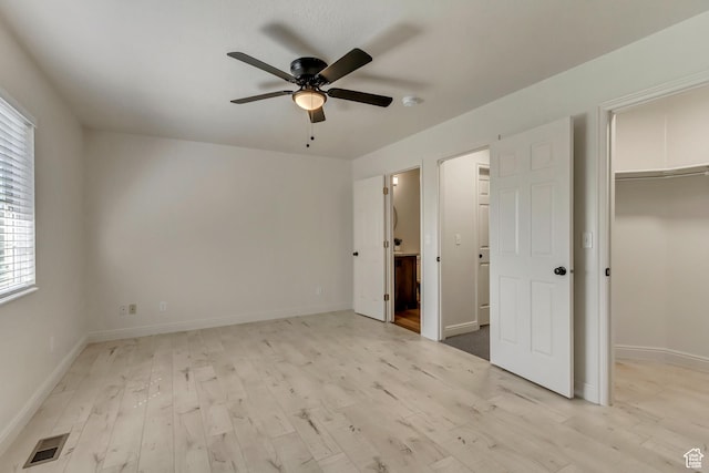 unfurnished bedroom with visible vents, a spacious closet, light wood-type flooring, and baseboards