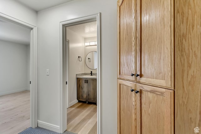 hallway featuring a sink, light wood-type flooring, and baseboards