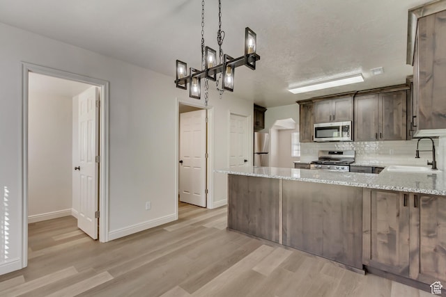 kitchen featuring tasteful backsplash, a sink, appliances with stainless steel finishes, light wood-style flooring, and light stone counters