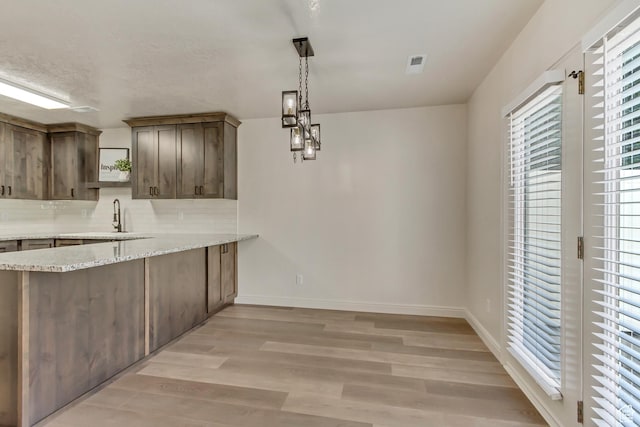 kitchen featuring light wood-style floors, light stone counters, a sink, decorative backsplash, and baseboards