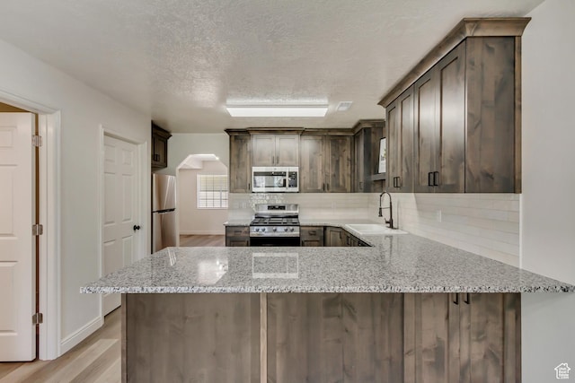 kitchen with stainless steel appliances, a sink, dark brown cabinets, and decorative backsplash