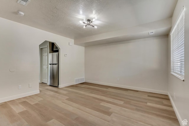 empty room featuring visible vents, light wood-style flooring, arched walkways, and baseboards