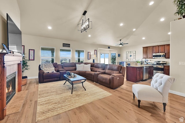 living room featuring recessed lighting, a tiled fireplace, light wood-type flooring, and ceiling fan with notable chandelier
