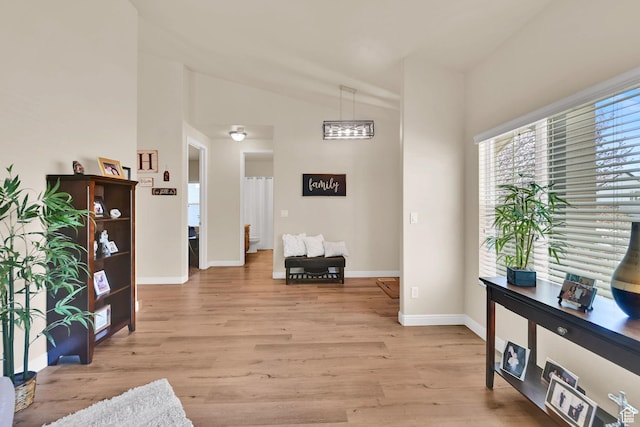 interior space featuring light wood-style flooring, baseboards, and lofted ceiling