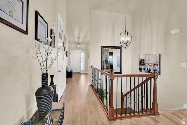 corridor featuring light wood-type flooring, an upstairs landing, a notable chandelier, and baseboards