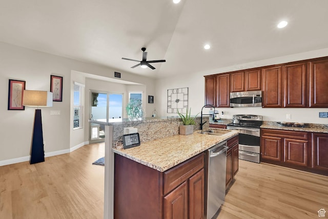 kitchen with a sink, a ceiling fan, stainless steel appliances, light wood-style flooring, and light stone counters