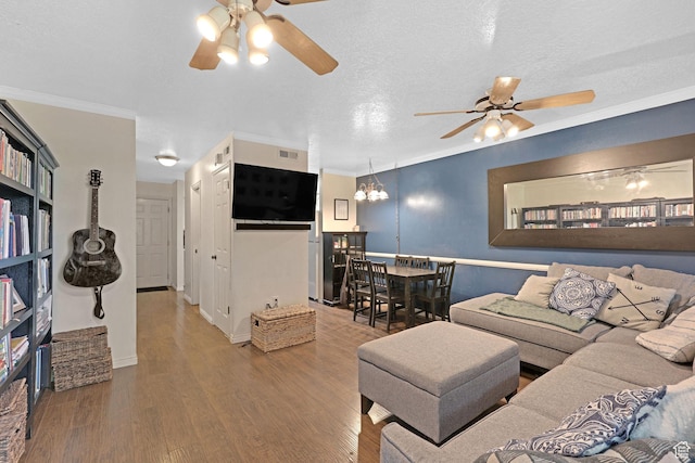 living room featuring ceiling fan with notable chandelier, wood finished floors, ornamental molding, and visible vents