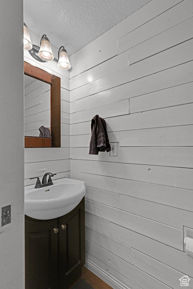 bathroom featuring a textured ceiling, wooden walls, and vanity