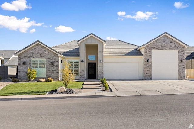 view of front of home with stone siding, a tile roof, a front lawn, an attached garage, and driveway