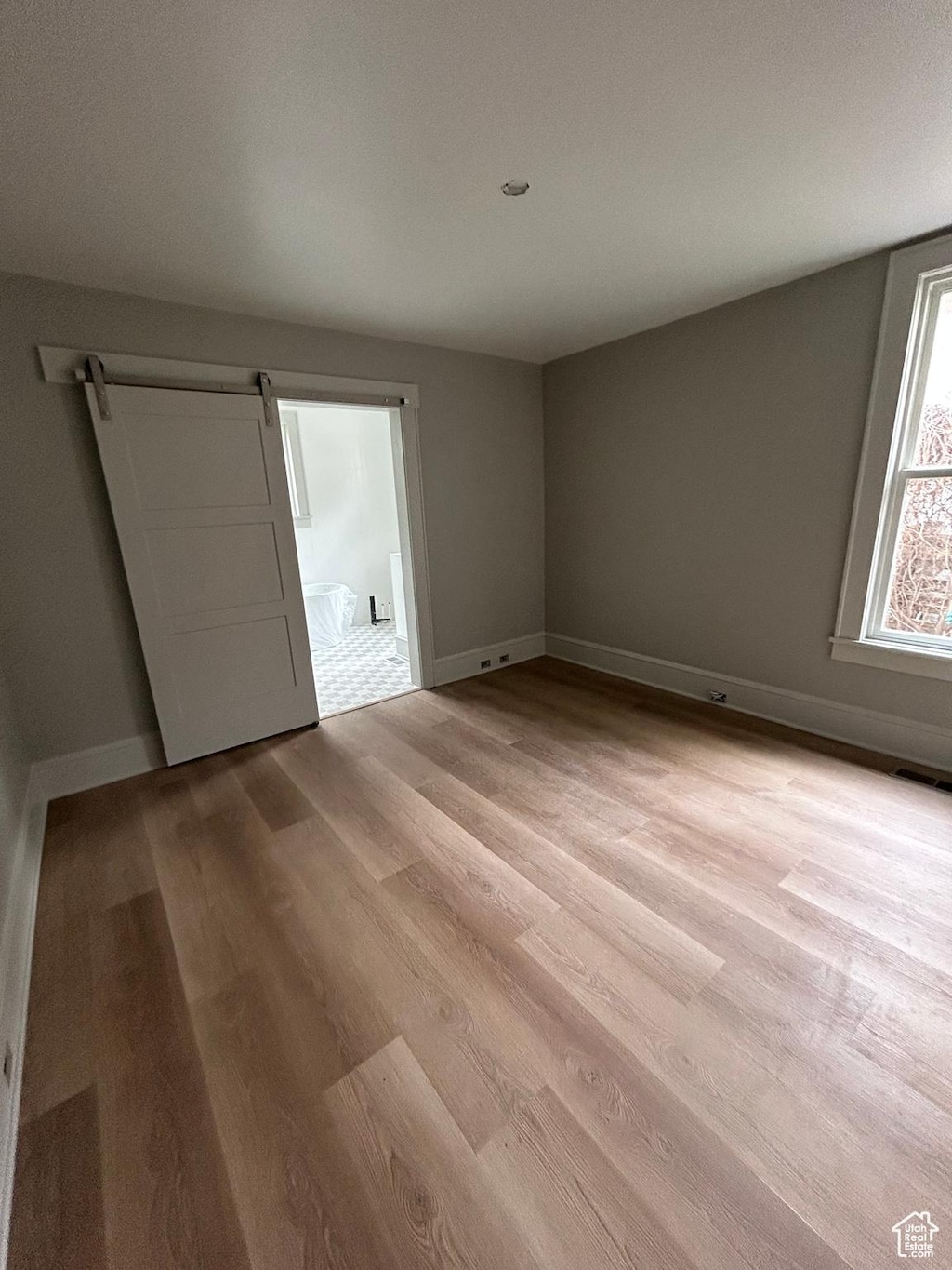 1161 E Bueno Ave, Salt Lake City, UT 84102 - empty room with a barn door, light wood-style floors, visible vents, and baseboards