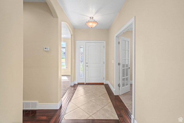entrance foyer with arched walkways, baseboards, visible vents, and tile patterned floors