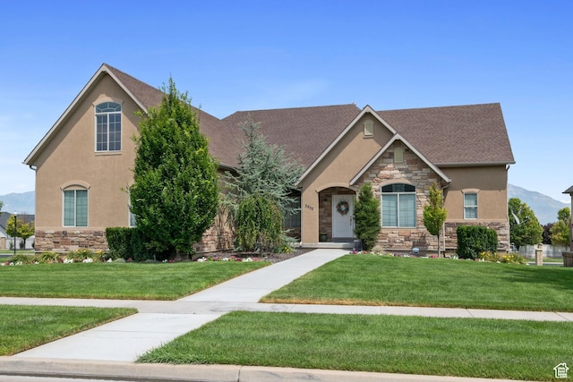 view of front of property featuring a mountain view, stucco siding, stone siding, and a front yard
