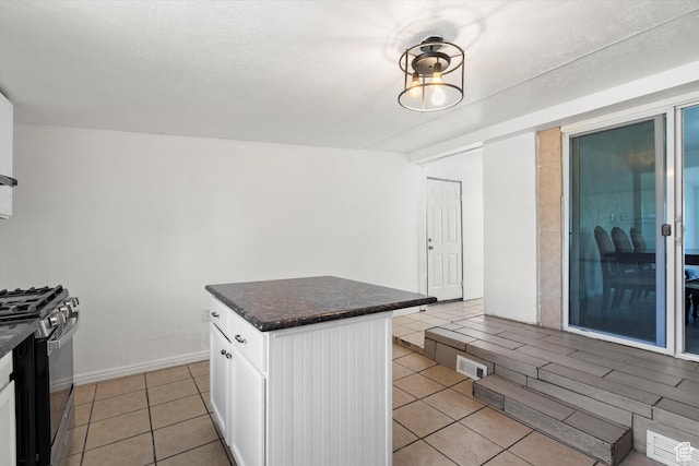 kitchen with light tile patterned floors, visible vents, a kitchen island, white cabinets, and black gas range oven