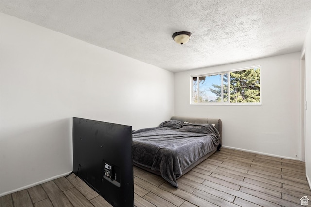 bedroom with a textured ceiling, wood finished floors, and baseboards