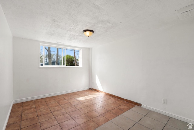 spare room with tile patterned flooring, a textured ceiling, and baseboards