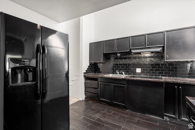 kitchen featuring tasteful backsplash, black appliances, under cabinet range hood, dark wood-type flooring, and a sink