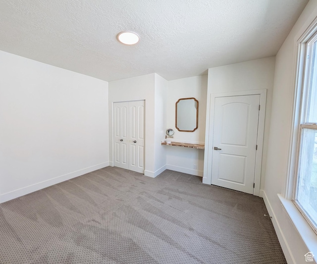 unfurnished bedroom featuring a textured ceiling, a closet, baseboards, and carpet