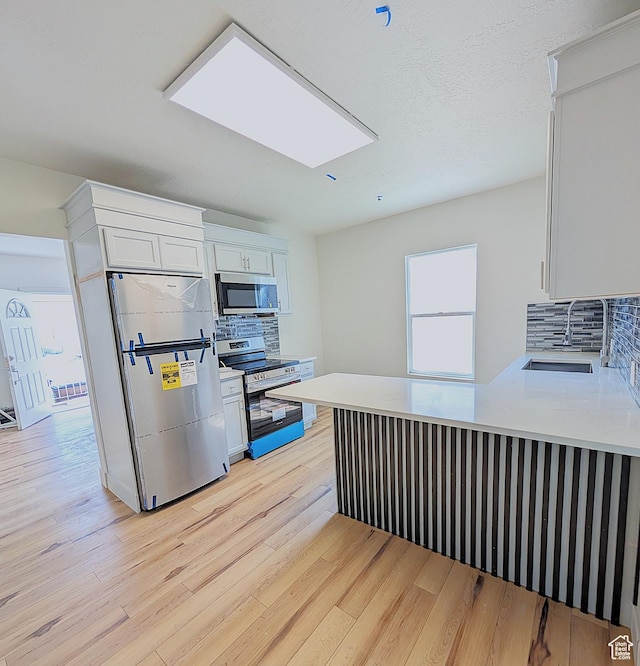 kitchen featuring light wood-style flooring, light countertops, backsplash, appliances with stainless steel finishes, and a sink