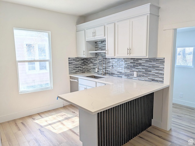 kitchen with white cabinets, a peninsula, light wood-style flooring, and a sink