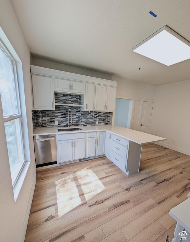 kitchen with dishwasher, a sink, light countertops, a peninsula, and decorative backsplash