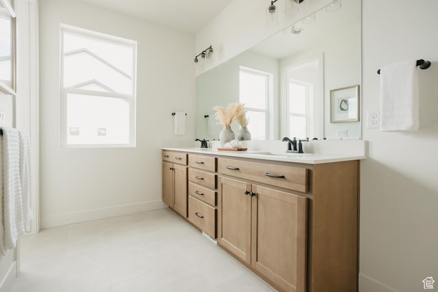 full bath with baseboards, double vanity, a sink, and plenty of natural light