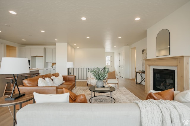 living area with recessed lighting, a glass covered fireplace, and light wood finished floors