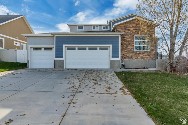 view of front of property with concrete driveway, stone siding, an attached garage, a front yard, and fence