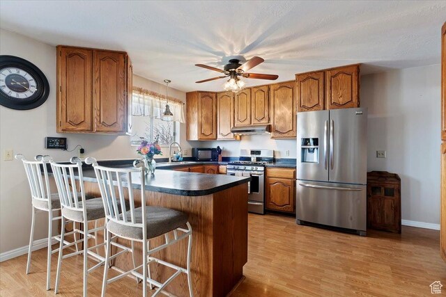 14883 S 3200 W, Bluffdale, UT 84065 - kitchen with dark countertops, a peninsula, under cabinet range hood, brown cabinets, and stainless steel appliances