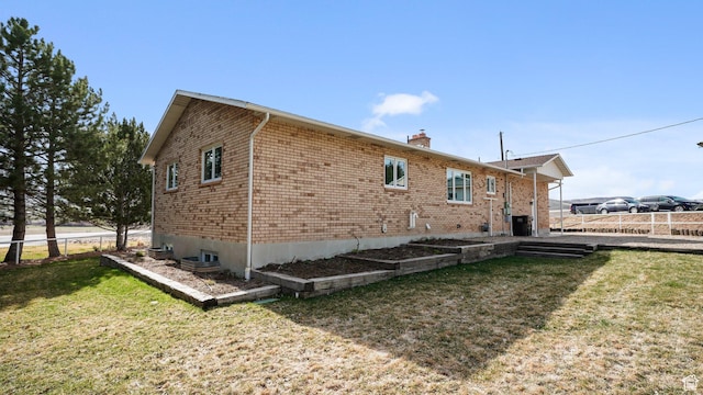 view of property exterior featuring brick siding, a chimney, fence, and a lawn
