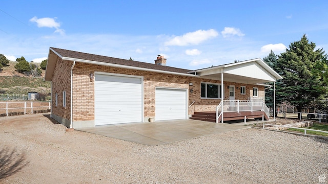 single story home with dirt driveway, a porch, brick siding, a chimney, and a garage