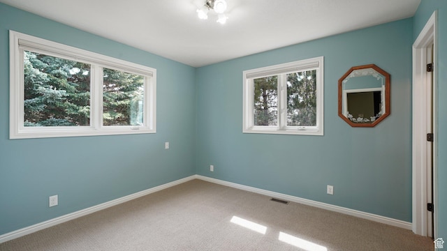 carpeted empty room featuring visible vents, baseboards, and a healthy amount of sunlight