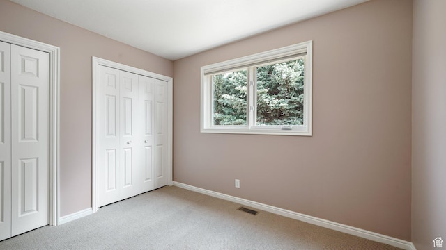 unfurnished bedroom with visible vents, baseboards, two closets, and light carpet