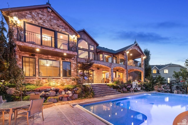 13879 S Standing Oak Dr E, Draper, UT 84020 - back of house with stairway, a patio area, stone siding, a balcony, and an outdoor pool