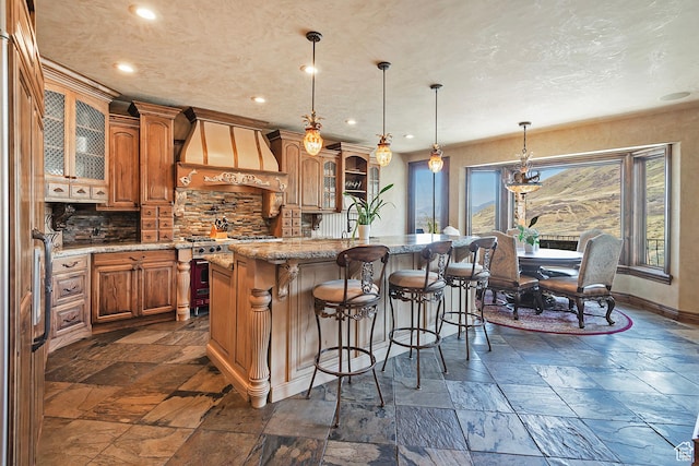 13879 S Standing Oak Dr E, Draper, UT 84020 - kitchen with high end range, stone tile floors, custom exhaust hood, brown cabinets, and backsplash
