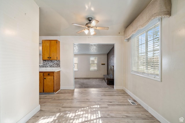 unfurnished living room with light wood-style floors, a fireplace, a ceiling fan, visible vents, and baseboards
