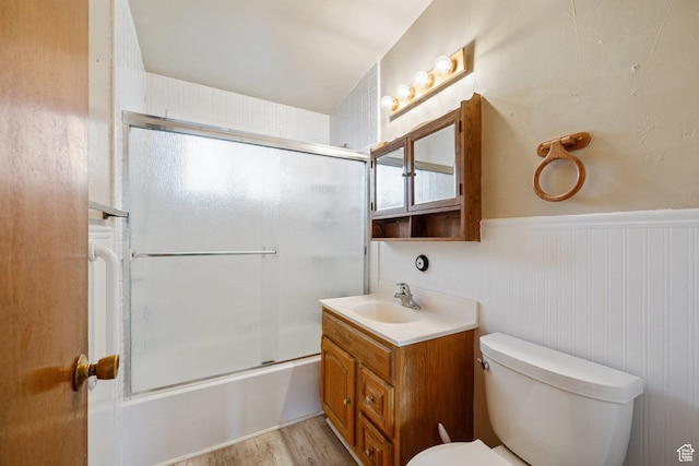 full bathroom featuring vanity, toilet, wood finished floors, enclosed tub / shower combo, and wainscoting