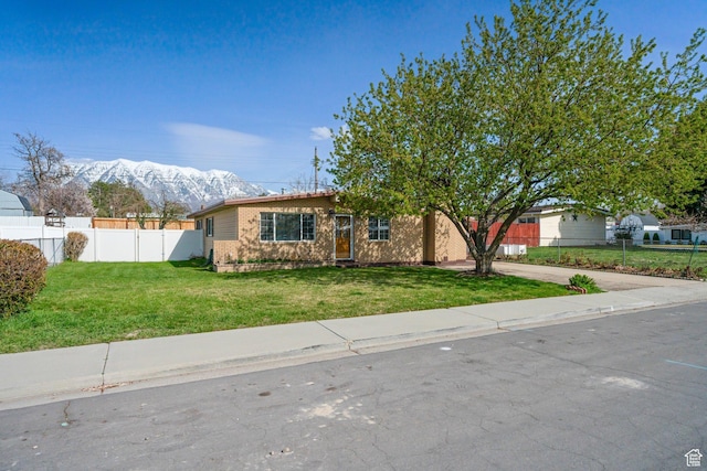 single story home featuring a mountain view, driveway, a front yard, brick siding, and fence