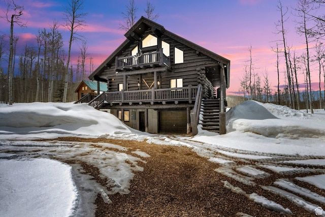 snow covered property featuring log exterior, stairs, a garage, and a balcony