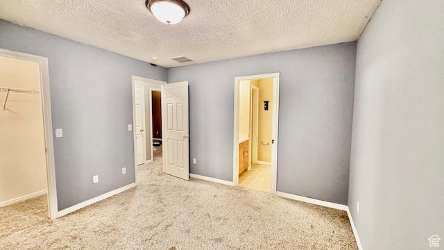 70 Teal Loop, Logan, UT 84321 - unfurnished bedroom with visible vents, a spacious closet, carpet, a textured ceiling, and ensuite bath