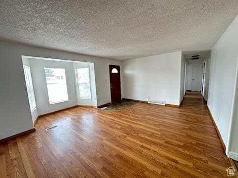 unfurnished living room featuring baseboards, wood finished floors, and a textured ceiling