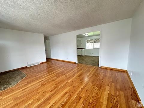 empty room featuring visible vents, a textured ceiling, baseboards, and wood finished floors