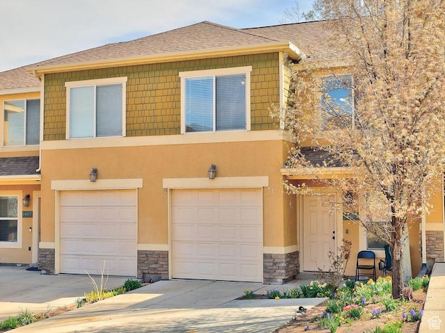 townhome / multi-family property featuring an attached garage, stone siding, stucco siding, driveway, and roof with shingles