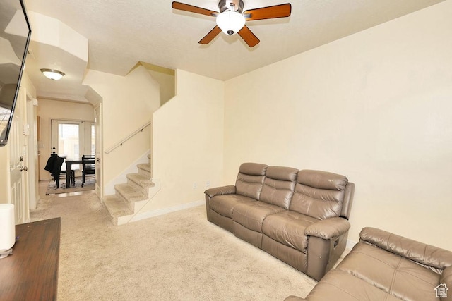 carpeted living room featuring baseboards, a ceiling fan, and stairs
