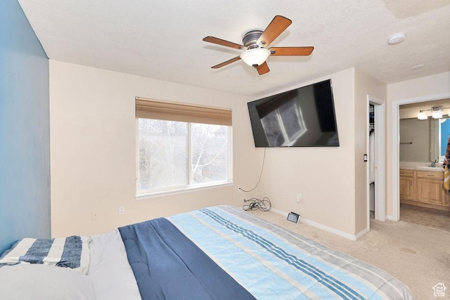 bedroom with ceiling fan, light colored carpet, ensuite bath, a sink, and baseboards