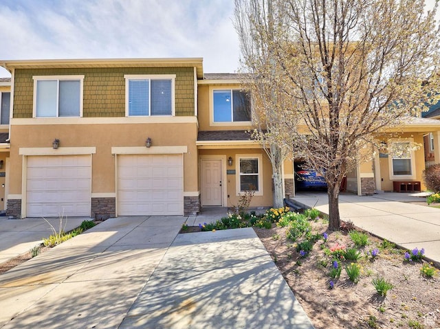 townhome / multi-family property with driveway, stucco siding, and stone siding
