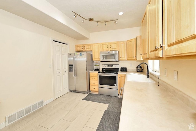kitchen featuring visible vents, a sink, light countertops, light brown cabinetry, and stainless steel appliances